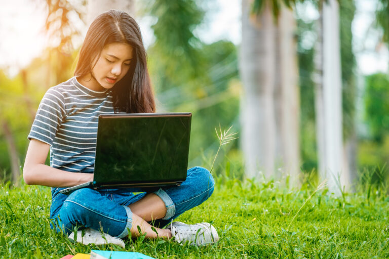 Dame zit in het gras met laptop op schoot.