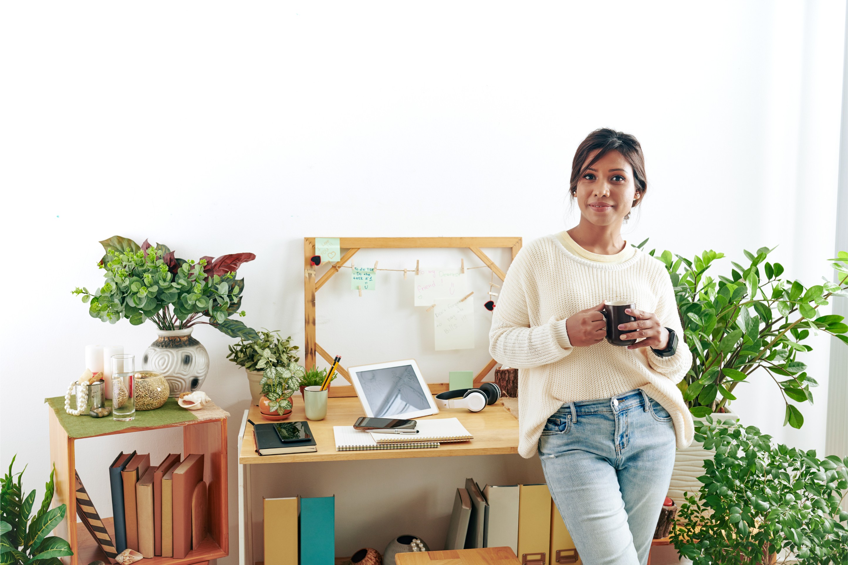 Dame thuis aan haar bureau met koffie. Tablet en twee telefoons op bureau. Internet thuis.